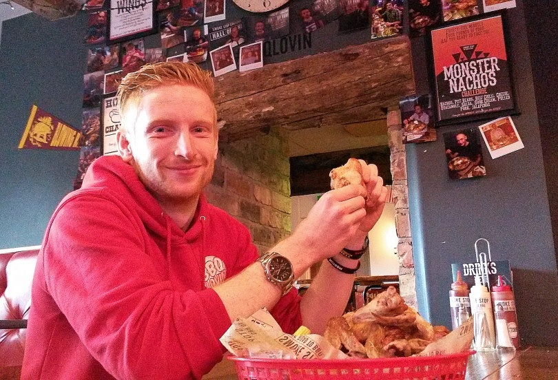 Stuart Sneade, the bar manager at Smoke Stop. the road to BBQ, attempts the King of the Wings challenge in front of the Hall of Fame at the American Smokehouse in Ford