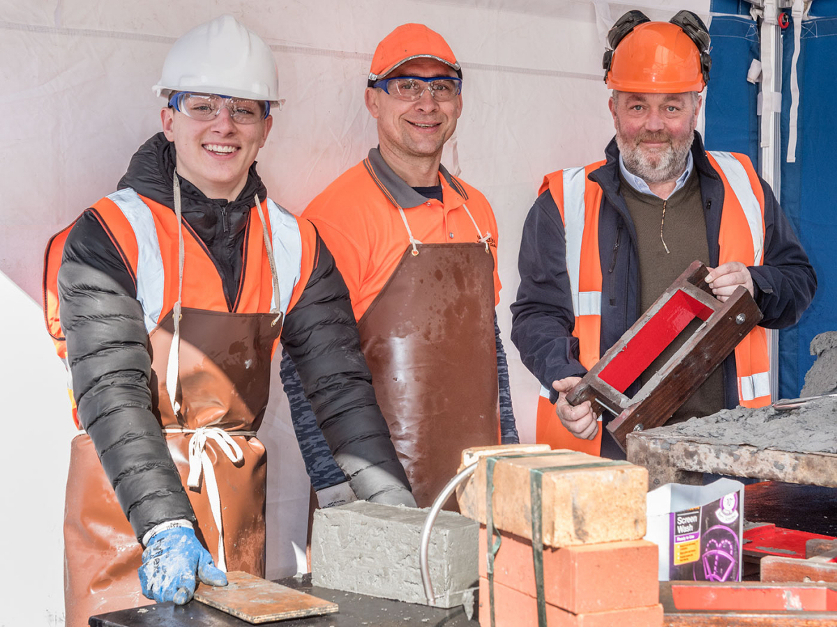 Shrewsbury Colleges Group student, Mateusz Kosinski; Northcot Brick demonstrator, Static Zbigneau; and Dale Mossfrom Northcot Brick, with the brick that Mateusz made which will go in the time capsule